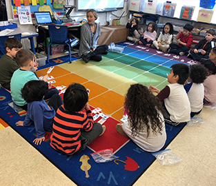 Students and their teacher sitting on a colorful rug